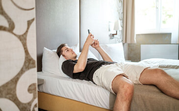 Mann liegt mit Smartphone auf Hotelbett